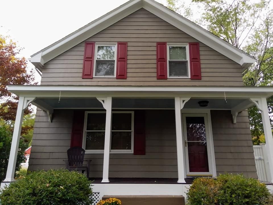 Tan clapboard home with a white porch and red shutters, repainted by Mario of Genesis Painting